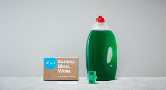 bluu Waschstreifen Verpackung neben grosser grüner Waschmittel Flasche mit Flüssigwaschmittel drin